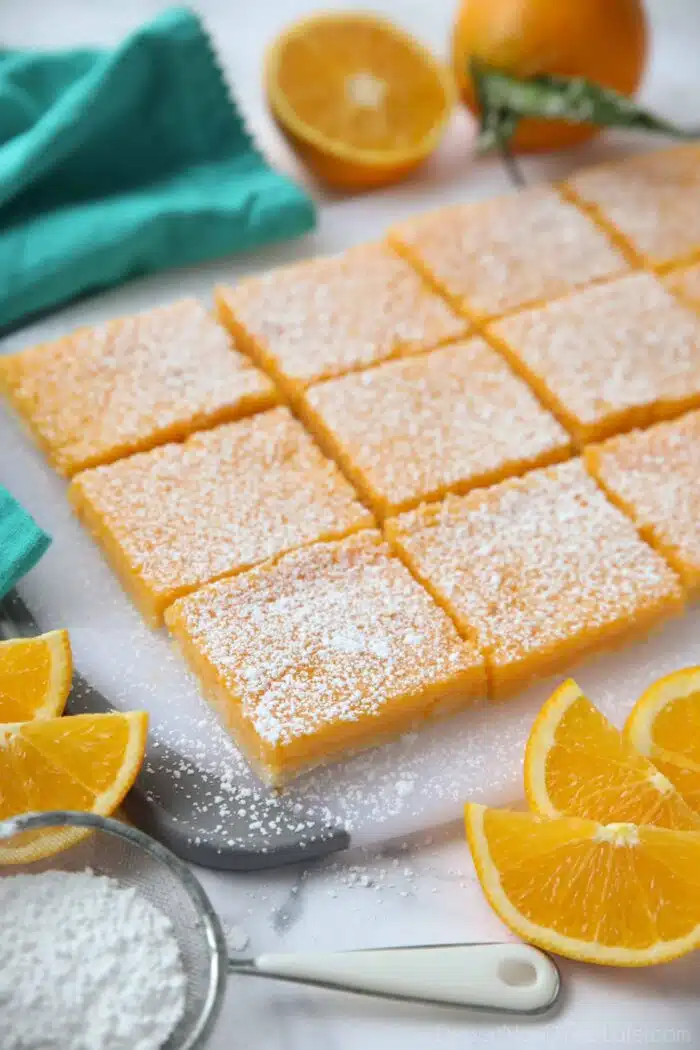 Squares of orange bars on a cutting board with powdered sugar on top.