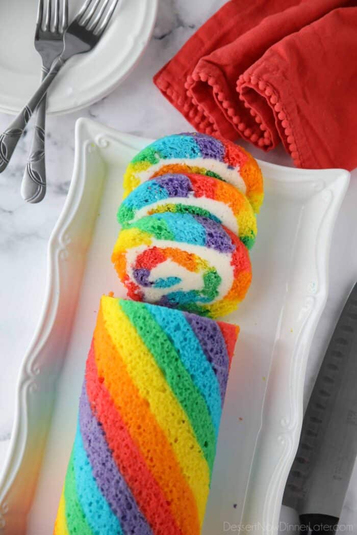 Rainbow cake roll on a platter with a few slices cut.