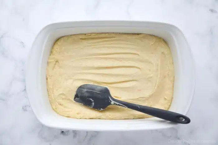 Spreading orange brownie batter into a 13x9-inch pan with a spatula.