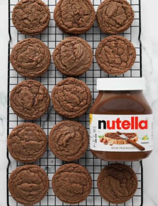 Nutella cookies on a wire cooling rack next to a jar of Nutella hazelnut spread with cocoa.