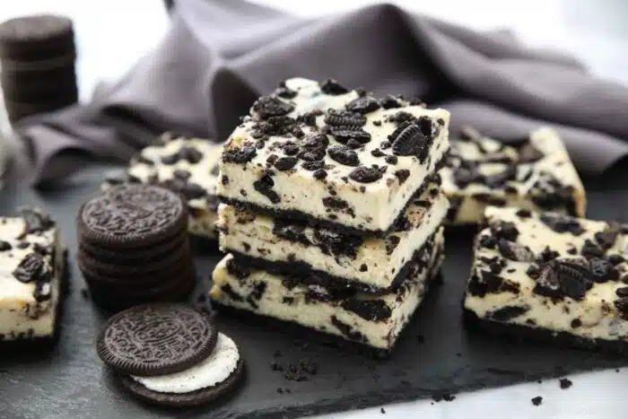 Three Oreo cheesecake bars stacked together next to more Oreos and cheesecake bars.