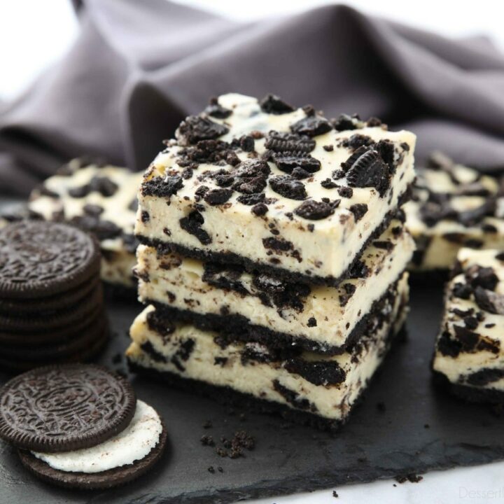 Three Oreo cheesecake bars stacked together next to more Oreos and cheesecake bars.