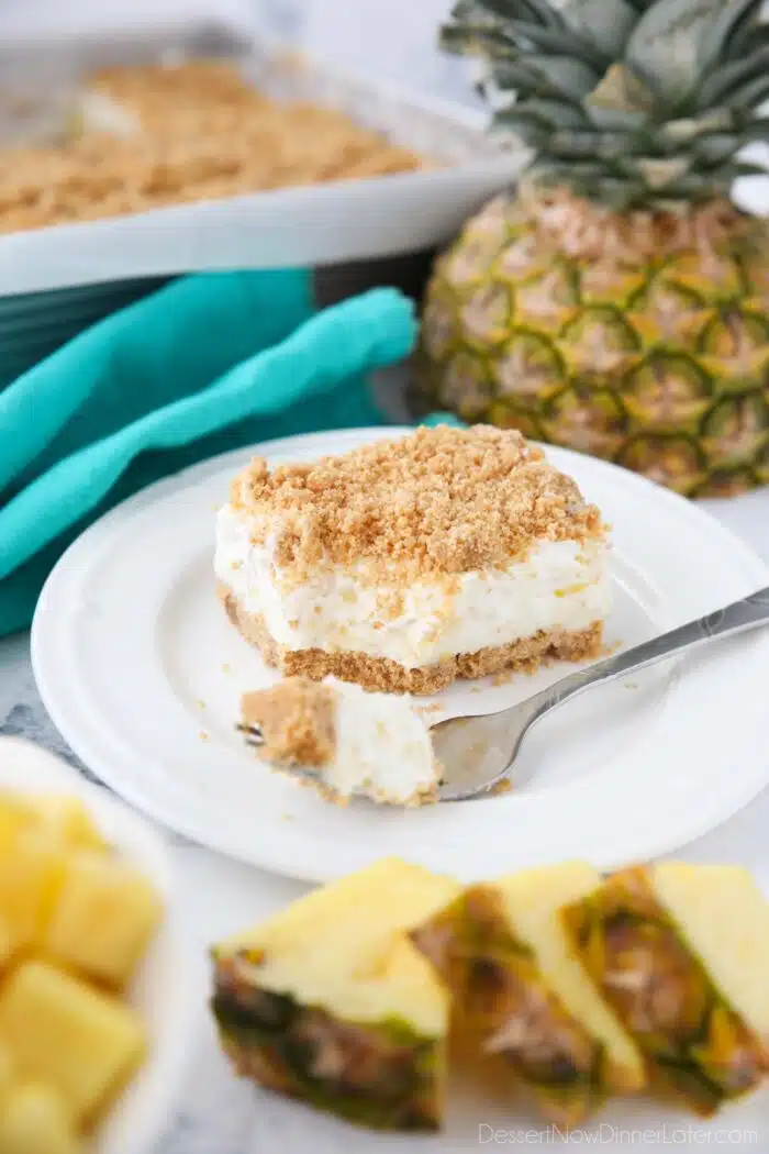 A slice of pineapple delight on a plate with a fork-full taken out. A creamy pineapple dream dessert with graham crackers, cream cheese, and whipped topping.