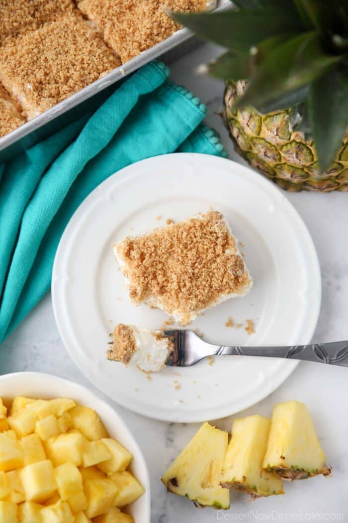 Top view of a rectangular slice of pineapple delight on a plate with a fork-full taken out.