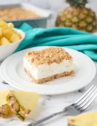 Side view of a slice of pineapple delight on a plate. A creamy pineapple dream dessert with buttery graham cracker crumbs.