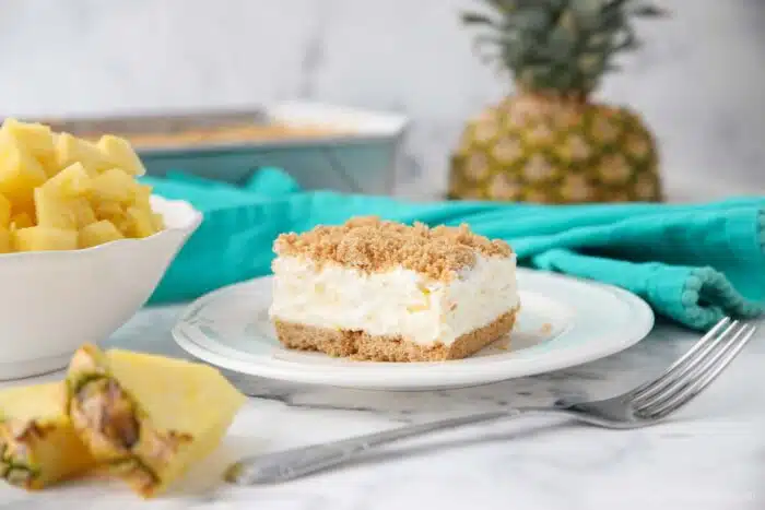 Square slice of pineapple delight on a plate consisting of a creamy pineapple filling sandwiched between graham cracker crumbs.