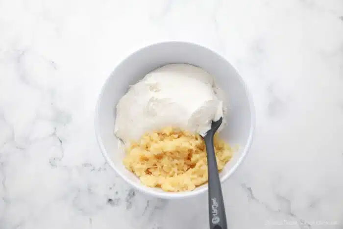 Folding crushed pineapple into whipped topping with a spatula.