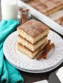 Stack of sopapilla cheesecake bars on a plate with cinnamon sticks.