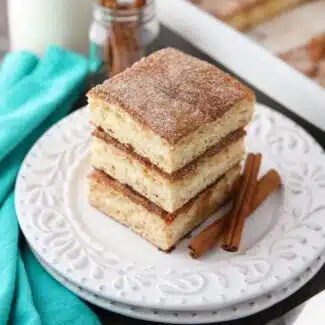 Stack of sopapilla cheesecake bars on a plate with cinnamon sticks.