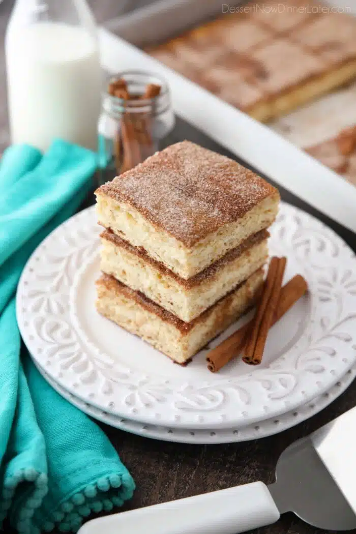 Stack of sopapilla cheesecake bars on a plate with cinnamon sticks.
