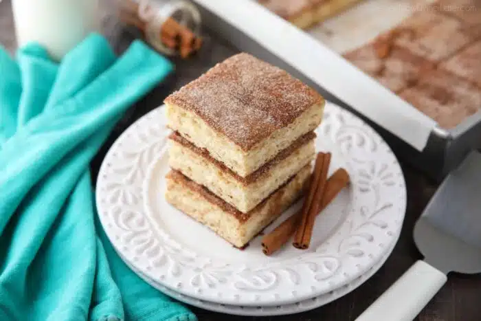 Stack of churro cheesecake bars on a plate with cinnamon sticks.