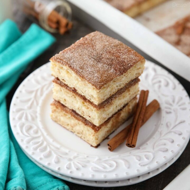 Stack of churro cheesecake bars on a plate with cinnamon sticks.