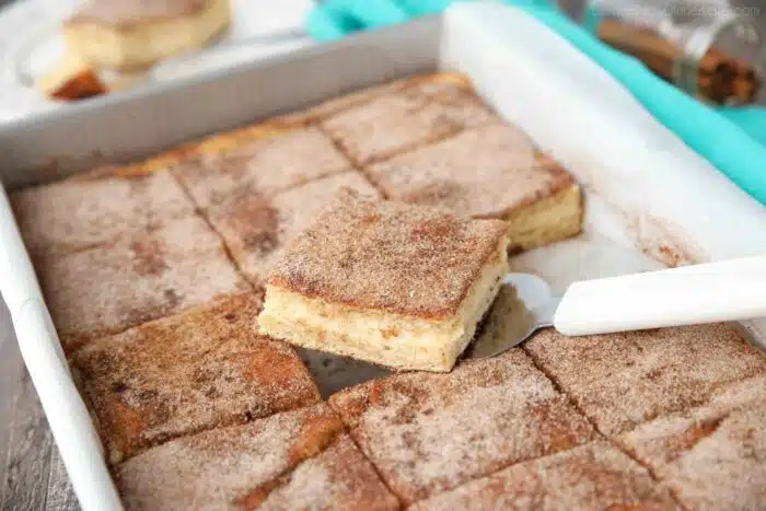 Spatula removing a piece of churro cheesecake bars from a pan.