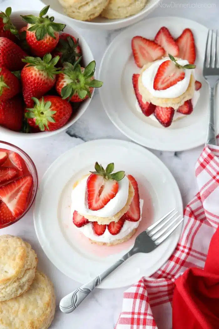 Top view of strawberry shortcake stacks on plates with biscuits, whipped cream, and strawberries.