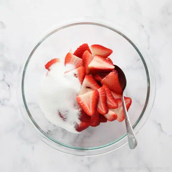 Sugar and sliced strawberries in a bowl.