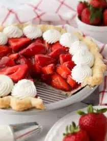 Fresh strawberry pie topped with whipped cream with a slice taken out of the pan.