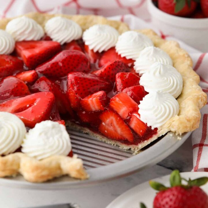 Fresh strawberry pie topped with whipped cream with a slice taken out of the pan.