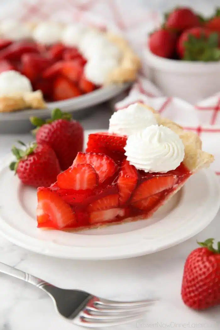 Slice of fresh strawberry pie on a plate with whipped cream piped on top.