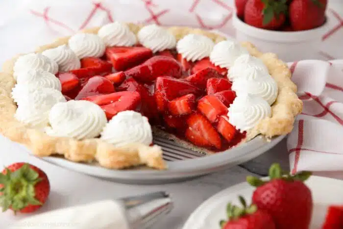 Fresh strawberry pie topped with whipped cream with a slice taken out of the pan.