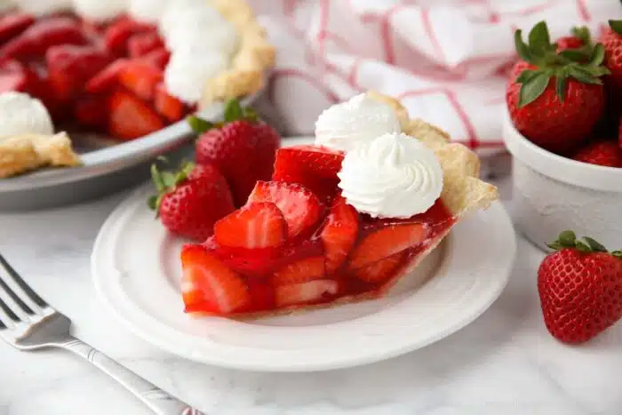 Slice of fresh strawberry pie on a plate with whipped cream piped on top.
