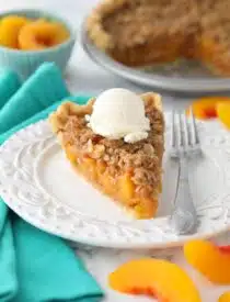 Slice of peach crumb pie on a plate with vanilla ice cream on top.