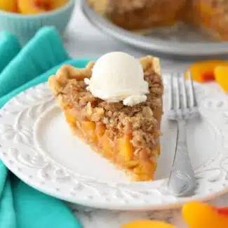 Slice of peach crumb pie on a plate with vanilla ice cream on top.