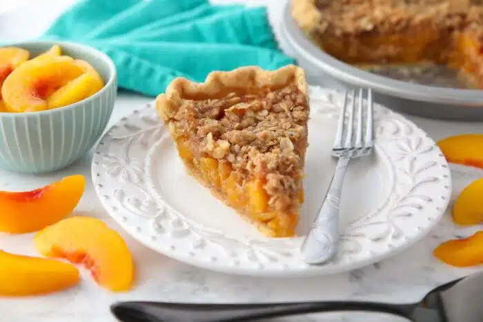 Slice of peach crumble pie on a plate with a fork.
