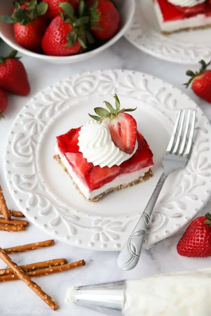 Piece of strawberry pretzel salad dessert on a plate garnished with whipped cream piped into a swirl with half of a strawberry.