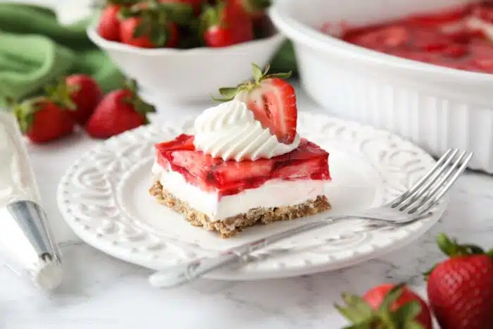 Piece of strawberry pretzel salad dessert on a plate topped with whipped cream and half of a strawberry.