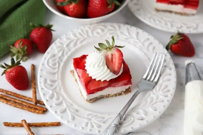 Piece of strawberry pretzel salad dessert on a plate garnished with whipped cream piped into a swirl with half of a strawberry.
