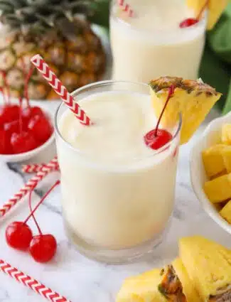 Virgin pina colada in a glass cup with a wedge of pineapple, a maraschino cherry, and a straw.