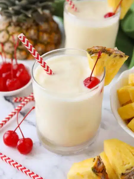 Virgin pina colada in a glass cup with a wedge of pineapple, a maraschino cherry, and a straw.