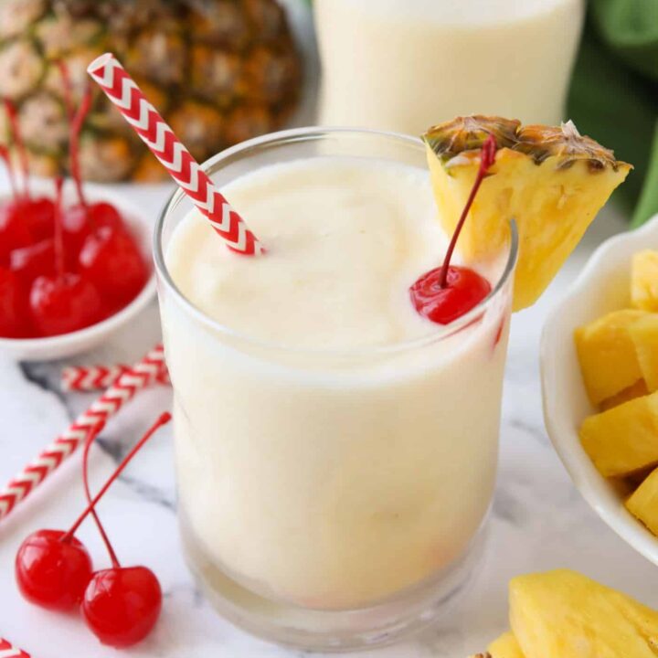 Virgin pina colada in a glass cup with a wedge of pineapple, a maraschino cherry, and a straw.