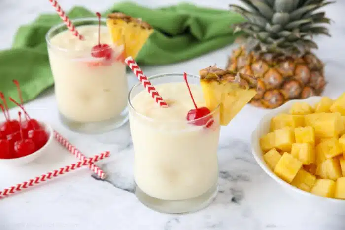 Virgin pina coladas in glass cups with a wedge of pineapple, a maraschino cherry, and a straw.