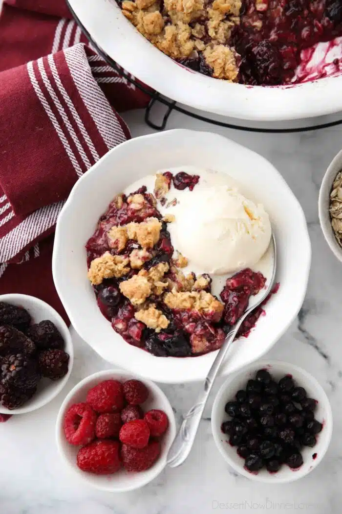 Bowl full of warm berry crisp with ice cream on top.