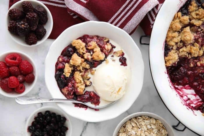 Bowl full of warm berry crisp with ice cream on top.