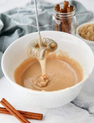 Cinnamon brown sugar glaze dripping off of a whisk into a bowl.