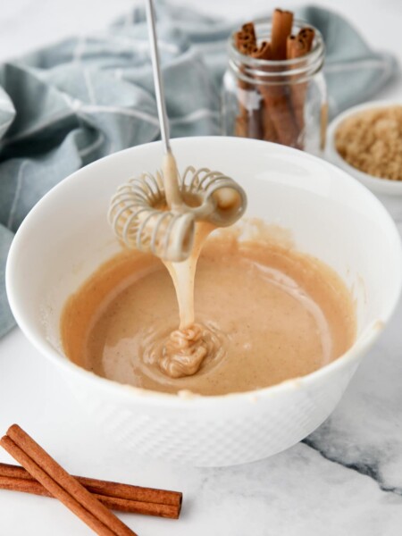 Cinnamon brown sugar glaze dripping off of a whisk into a bowl.