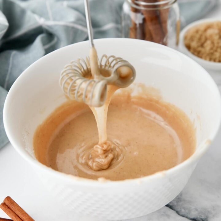 Cinnamon brown sugar glaze dripping off of a whisk into a bowl.