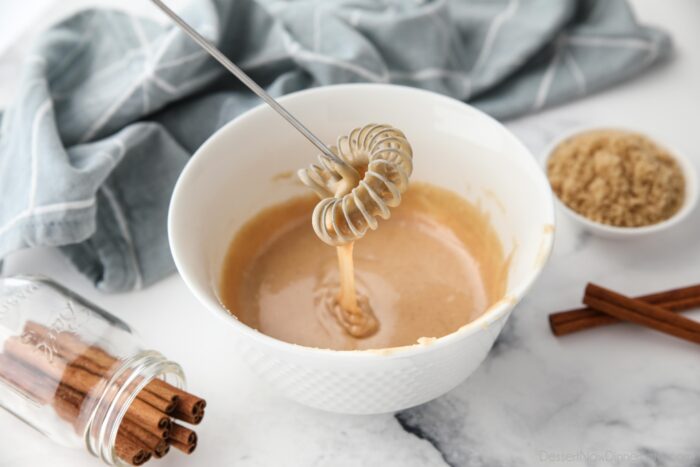 Cinnamon brown sugar glaze dripping off of a whisk into a bowl.