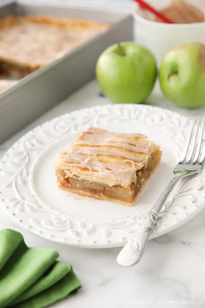 Slice of apple slab pie on a plate with maple glaze drizzled on top.