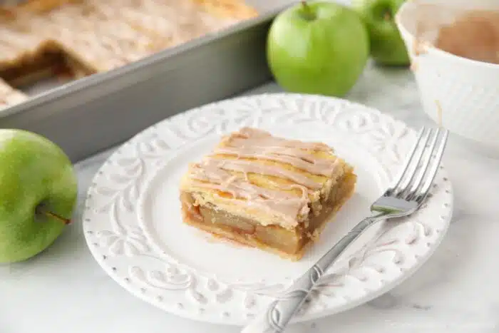 Slice of apple slab pie on a plate with maple glaze drizzled on top.