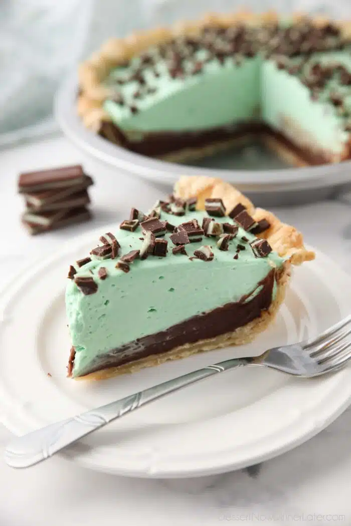Slice of chocolate mint pie on a plate with layers of pastry crust, chocolate ganache, mint no bake cheesecake, and chopped Andes mints.