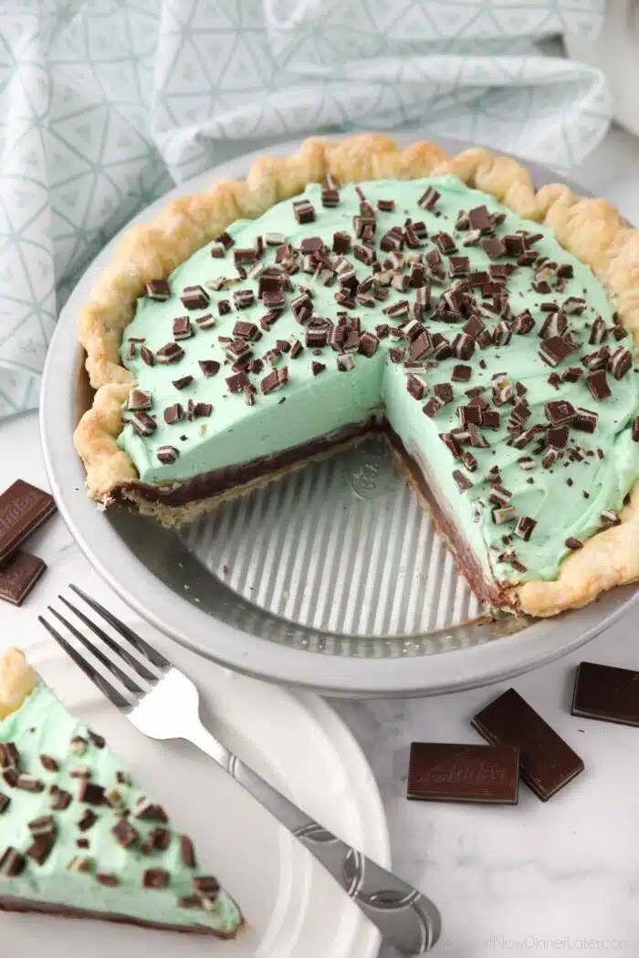 Chocolate mint pie in pan with layers of pastry crust, chocolate ganache, mint no bake cheesecake, and chopped Andes mints.