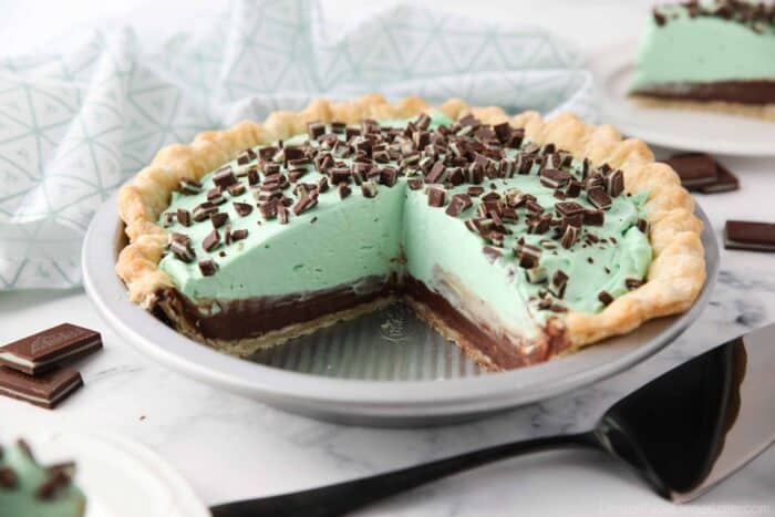 Chocolate mint pie in pan with layers of pastry crust, chocolate ganache, mint no bake cheesecake, and chopped Andes mints.
