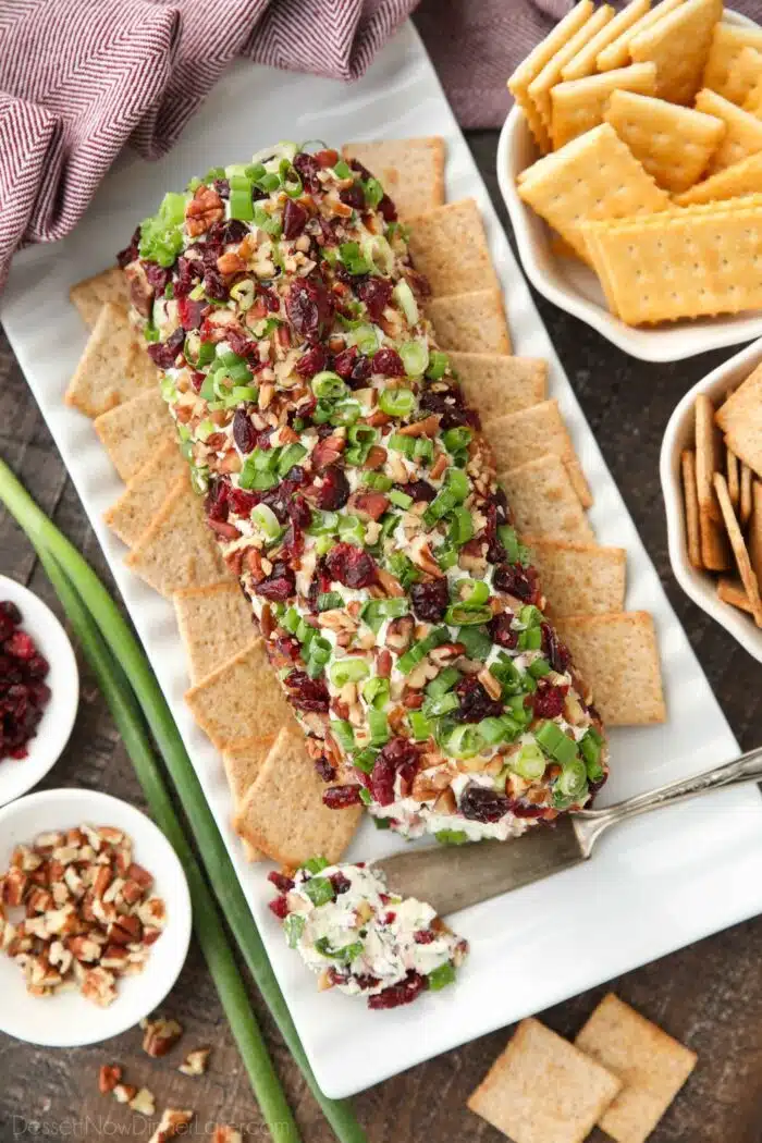 Top view of cranberry pecan cheeseball shaped into a log on a platter with crackers.