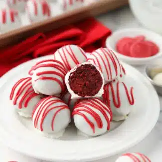 Red Velvet Truffles on a plate with one cut open showing the red cake inside of the white chocolate shell.
