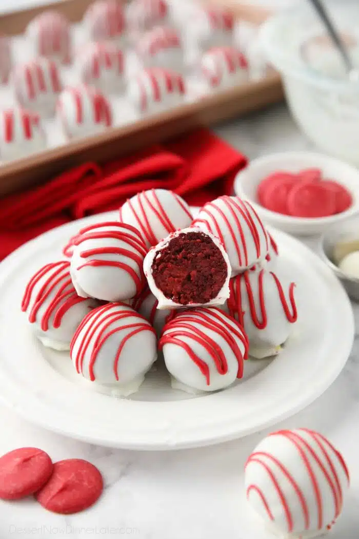 Red Velvet Truffles on a plate with one cut open showing the red cake inside of the white chocolate shell.