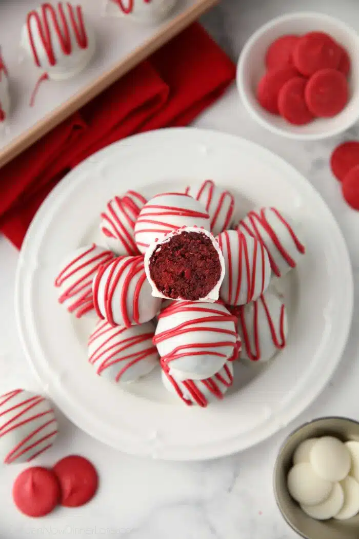 Red Velvet Cake Truffles on a plate with one cut open showing the red cake inside of the white chocolate shell.