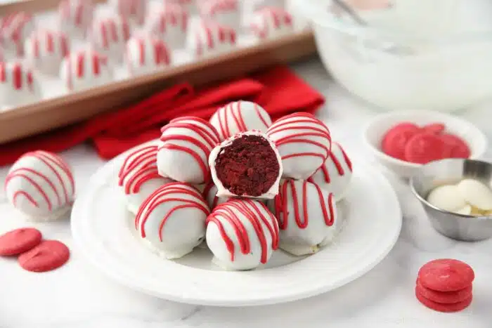 Red Velvet Truffles on a plate with one cut open showing the red cake inside of the white chocolate shell.